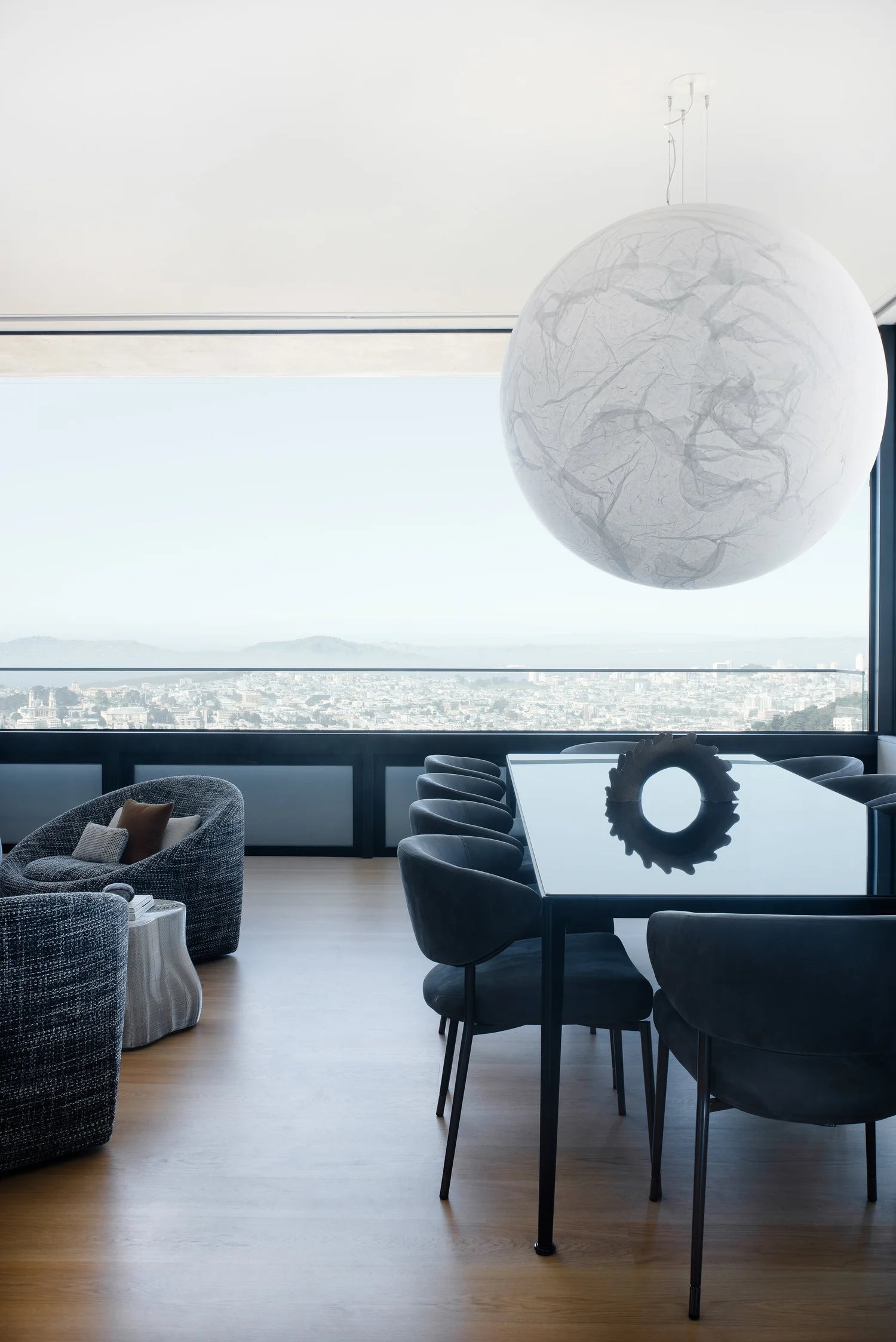 Modern interior with a large conference table, round white pendant light, black chairs, and a large window.