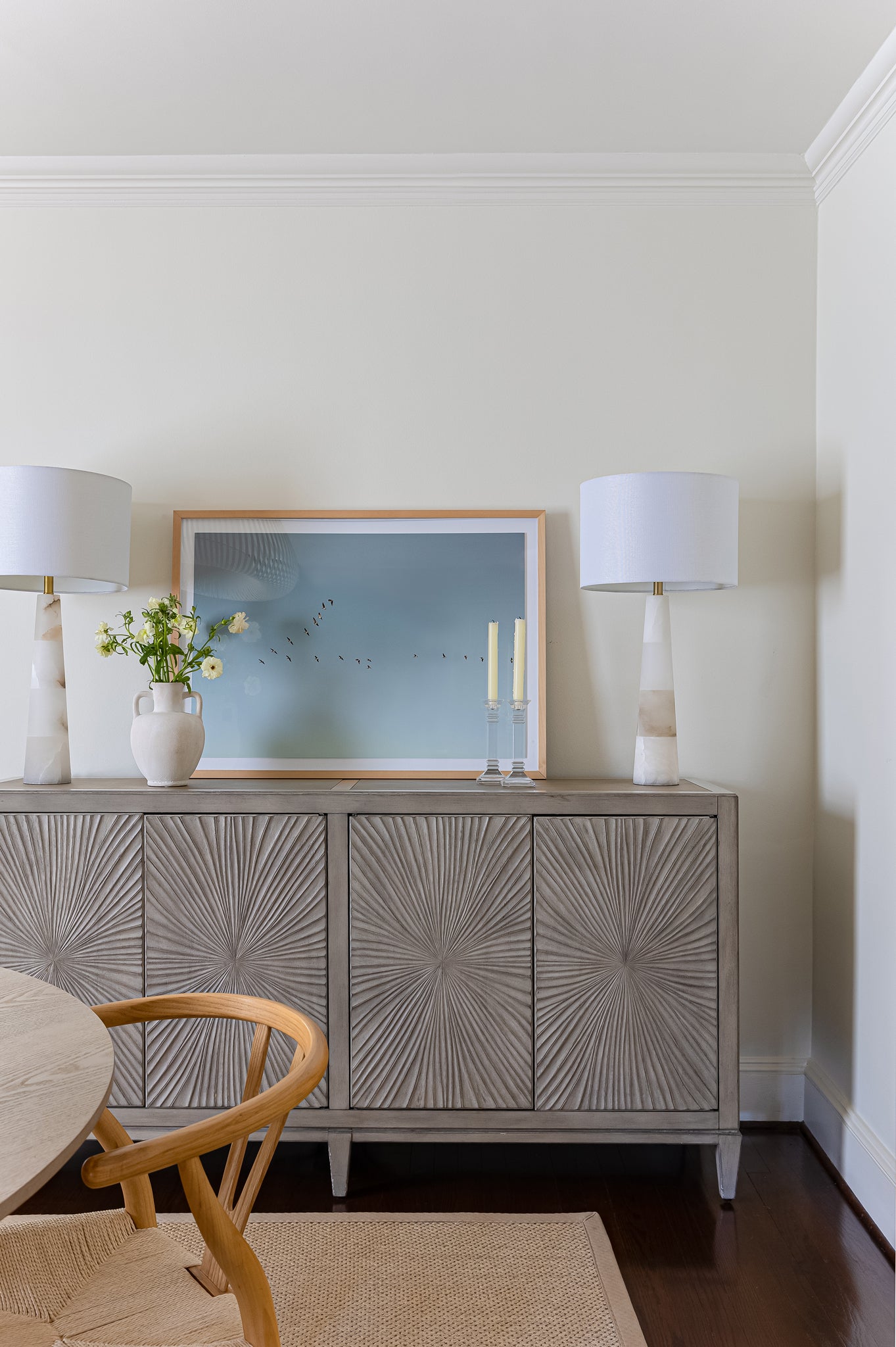 Framed photograph of birds flying in a V in blue sky on console table with lamps, candles, and flowers