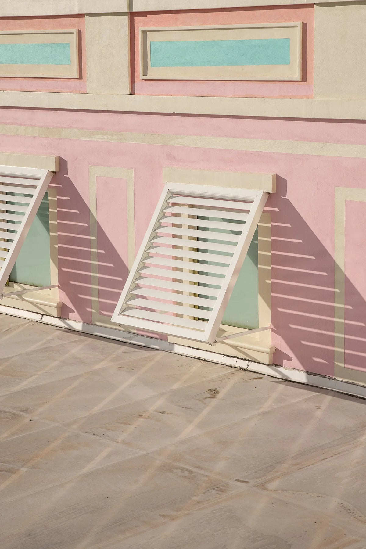 Pastel-colored building facade with white shutters on a stone pavement.