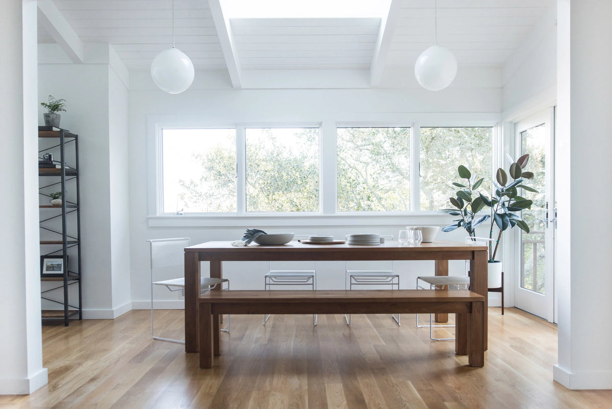 Modern kitchen with wooden dining table and bench, large windows, and white walls.