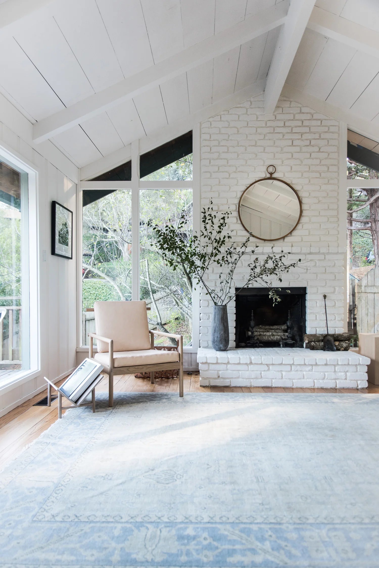 Living room with white brick fireplace, large windows, and a blue rug.
