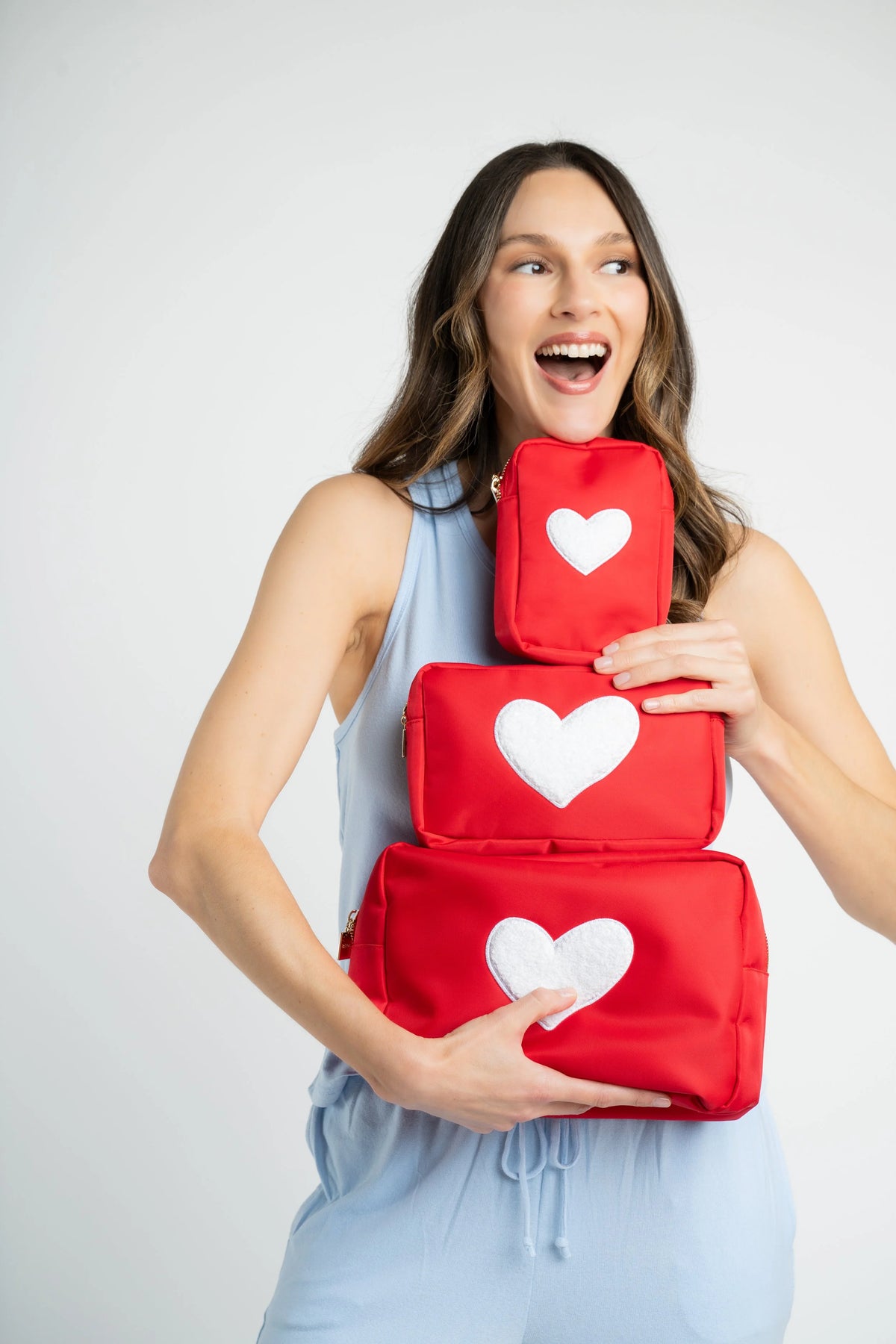 Woman holding three red pouches with white hearts on a white background