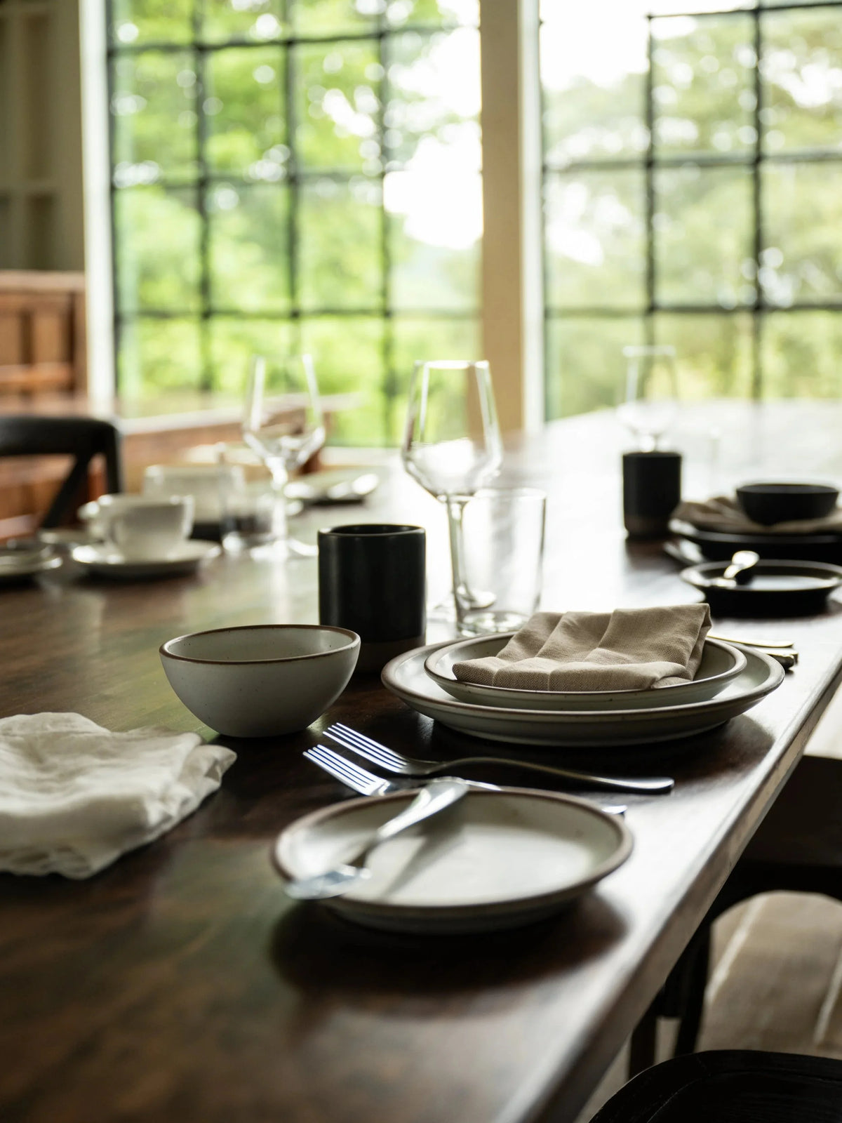 Dining table set with plates, glasses, and cutlery in a room with large windows.