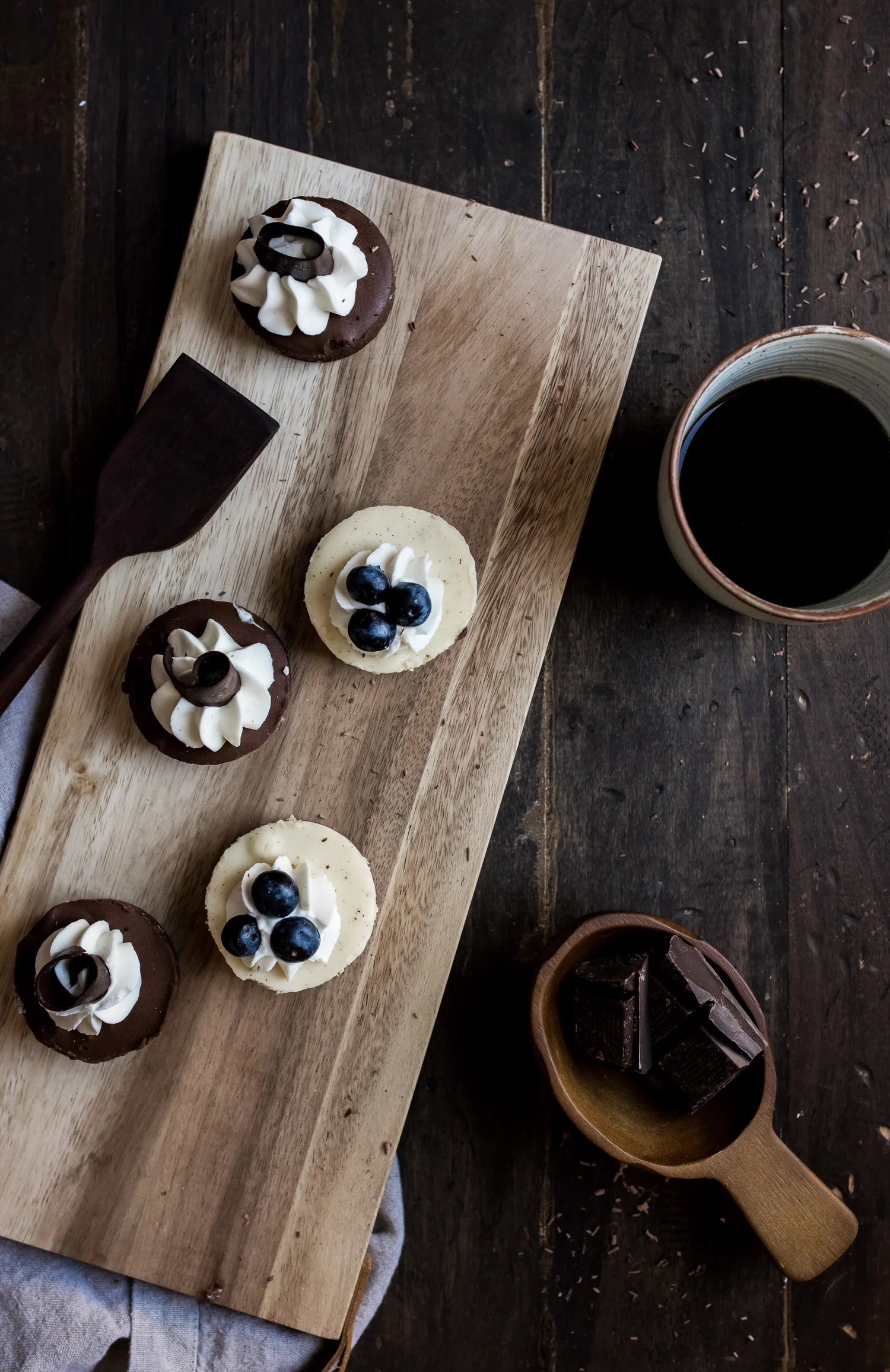 Wooden board with dessert items and a cup of coffee on a dark wooden surface