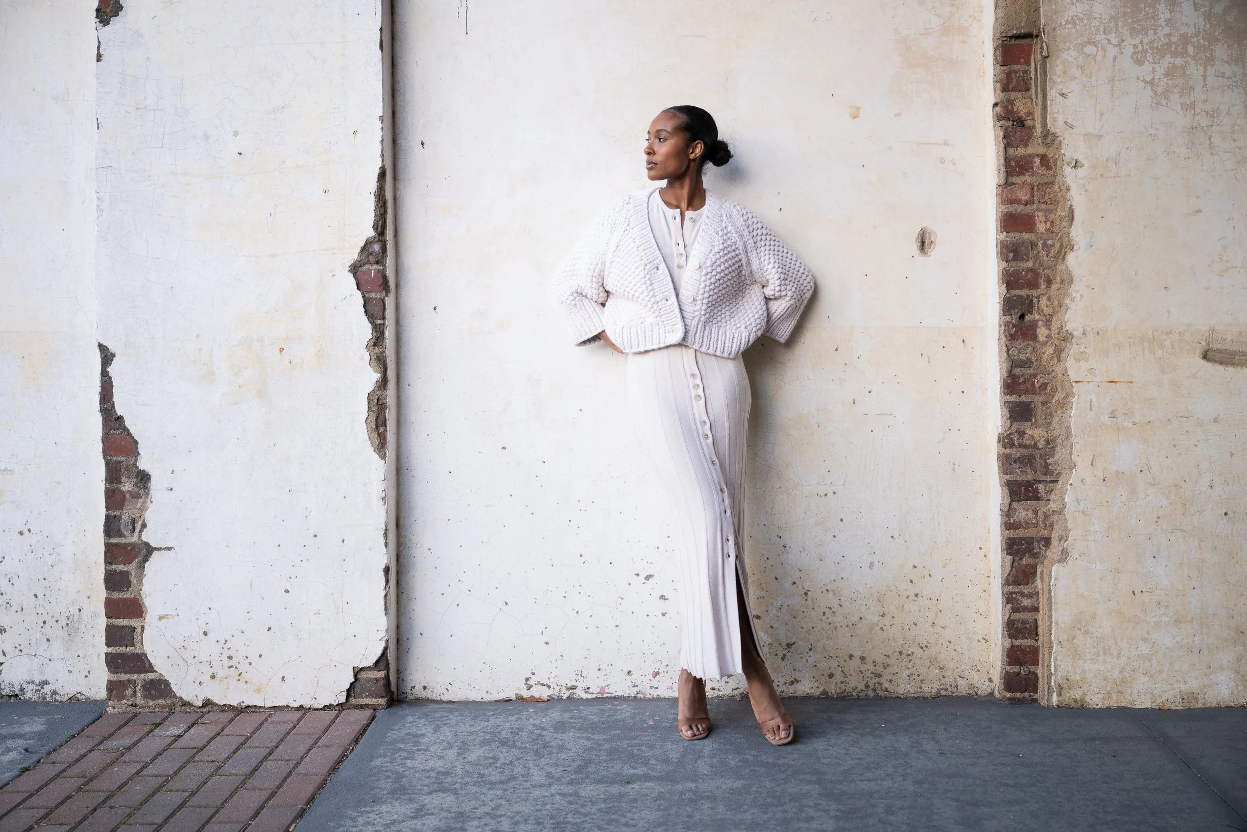 Woman in a white outfit standing against a textured wall.