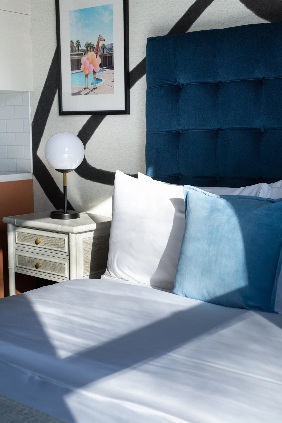 Bedroom with a blue upholstered headboard, white bedding, and a nightstand with a lamp.