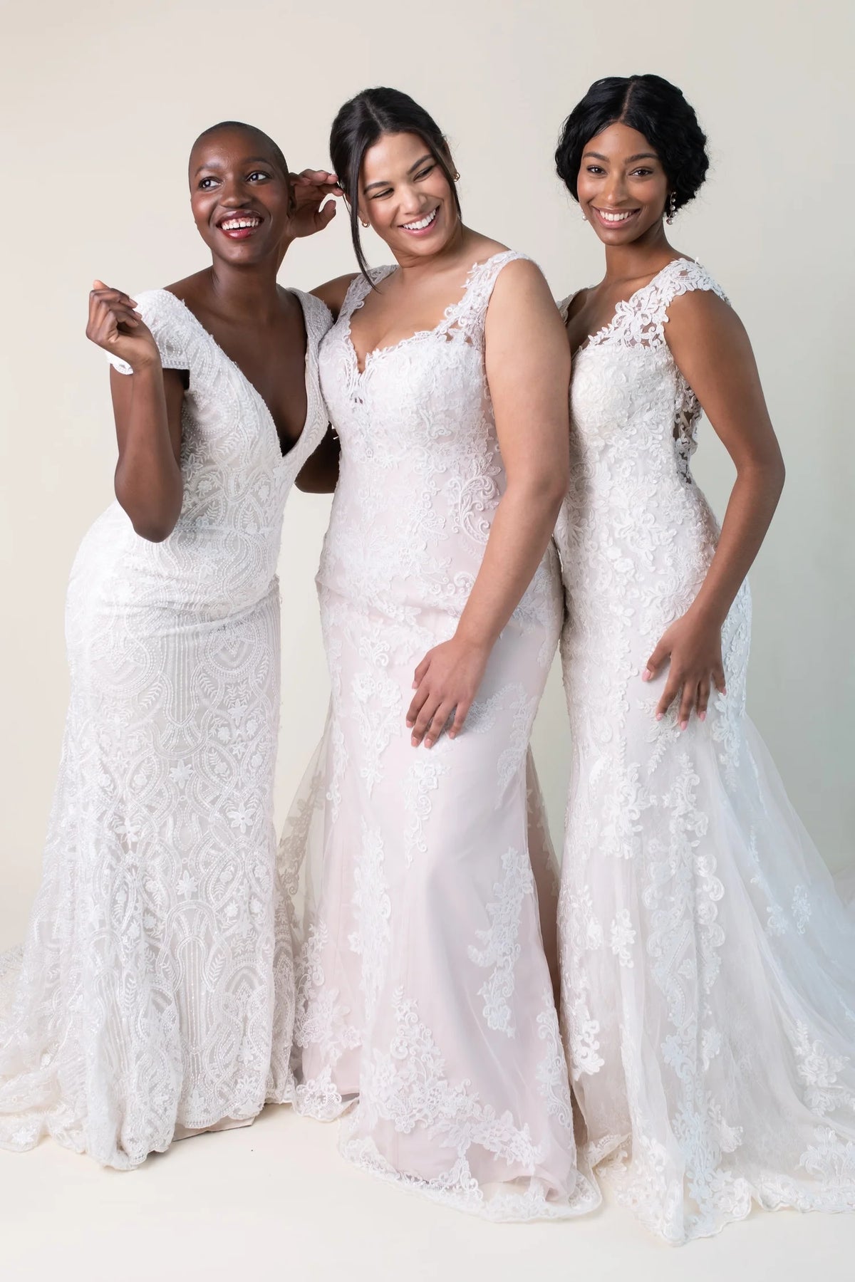 Three women wearing white bridal gowns laughing together