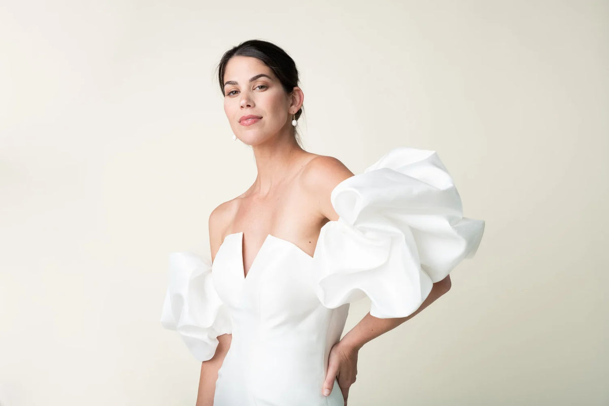 Woman wearing a white off-shoulder dress with ruffled sleeves against a plain background