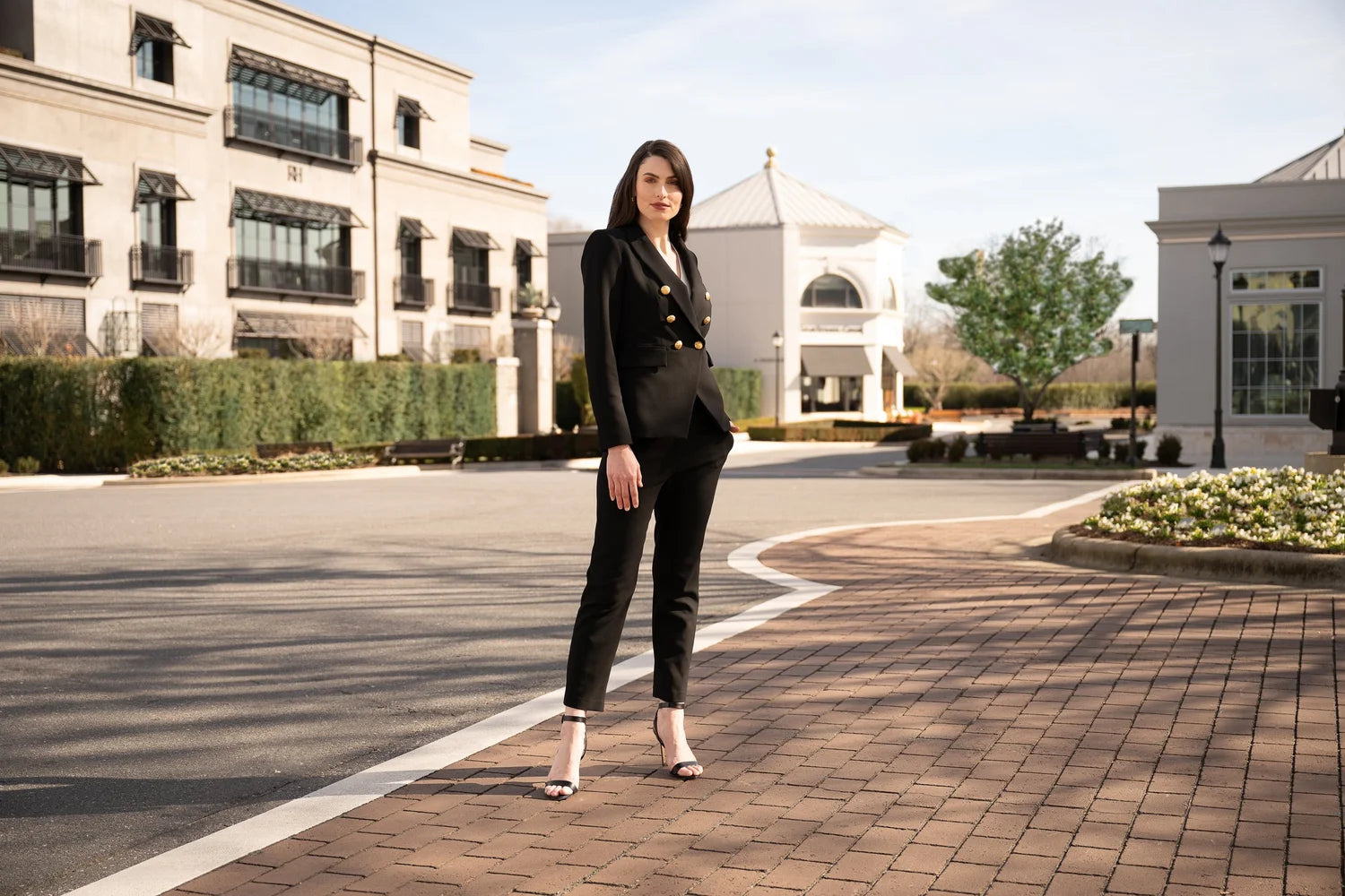 Woman in a black suit standing on a brick path in front of a building.