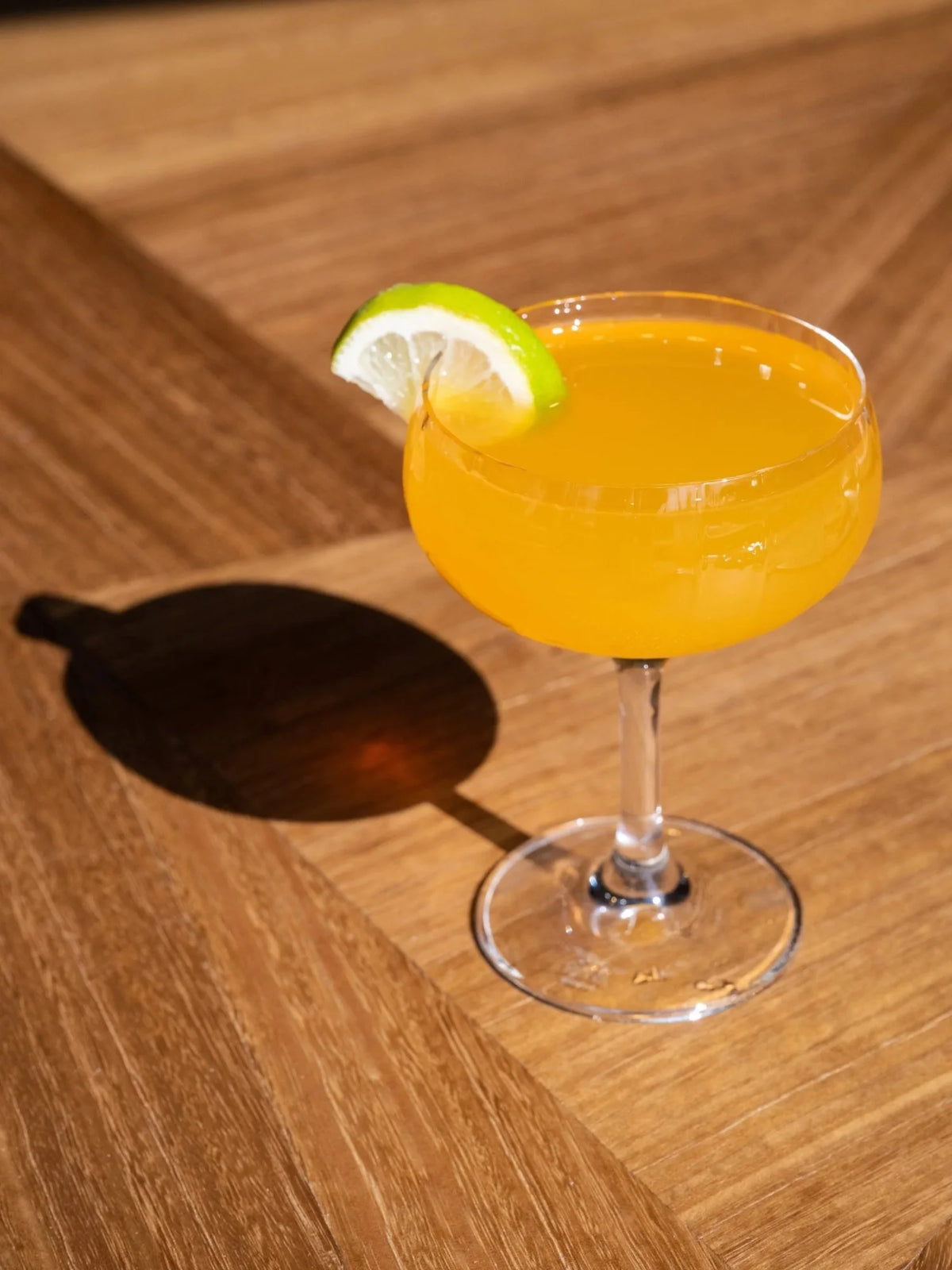 Bright yellow cocktail with lime wedge in stemmed glass on wooden table