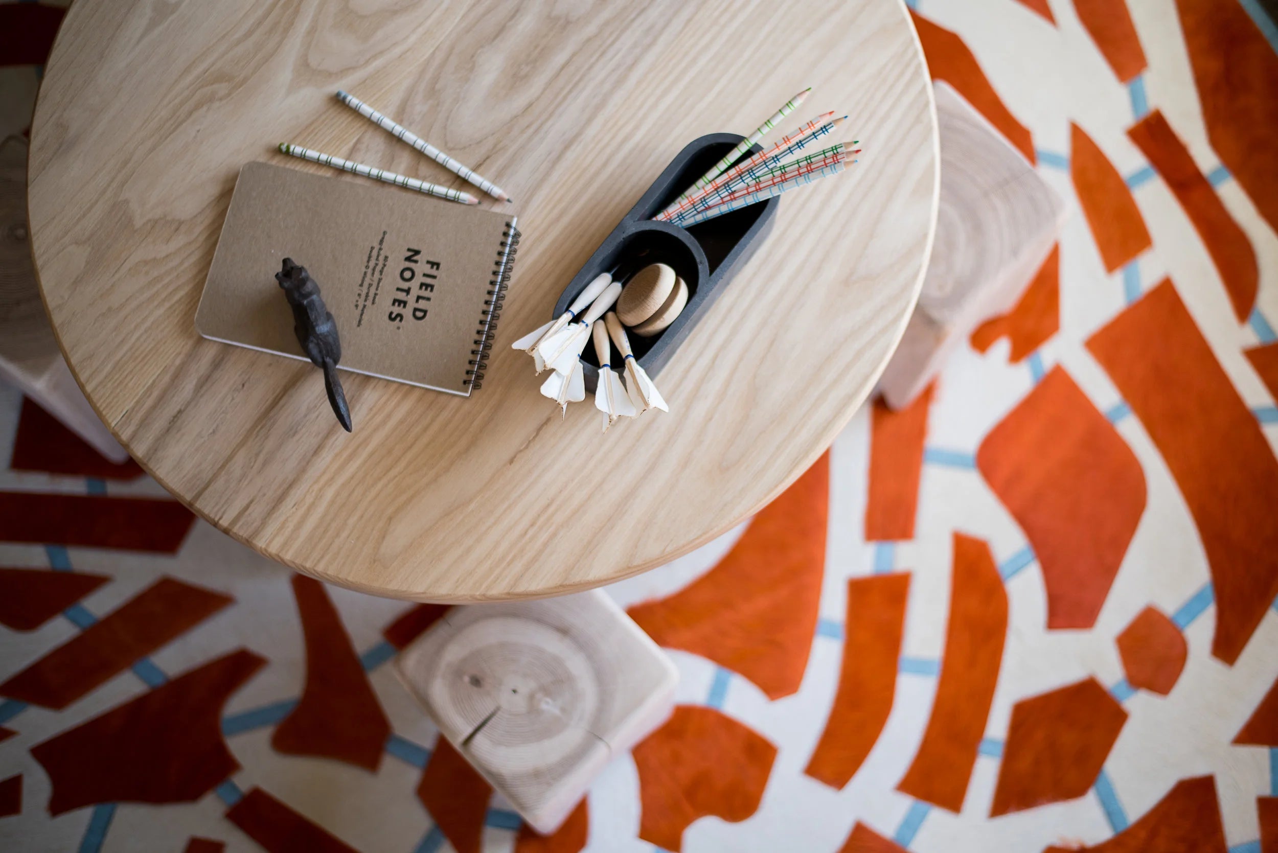 Round wooden table with notebooks and a small plant on an orange patterned rug