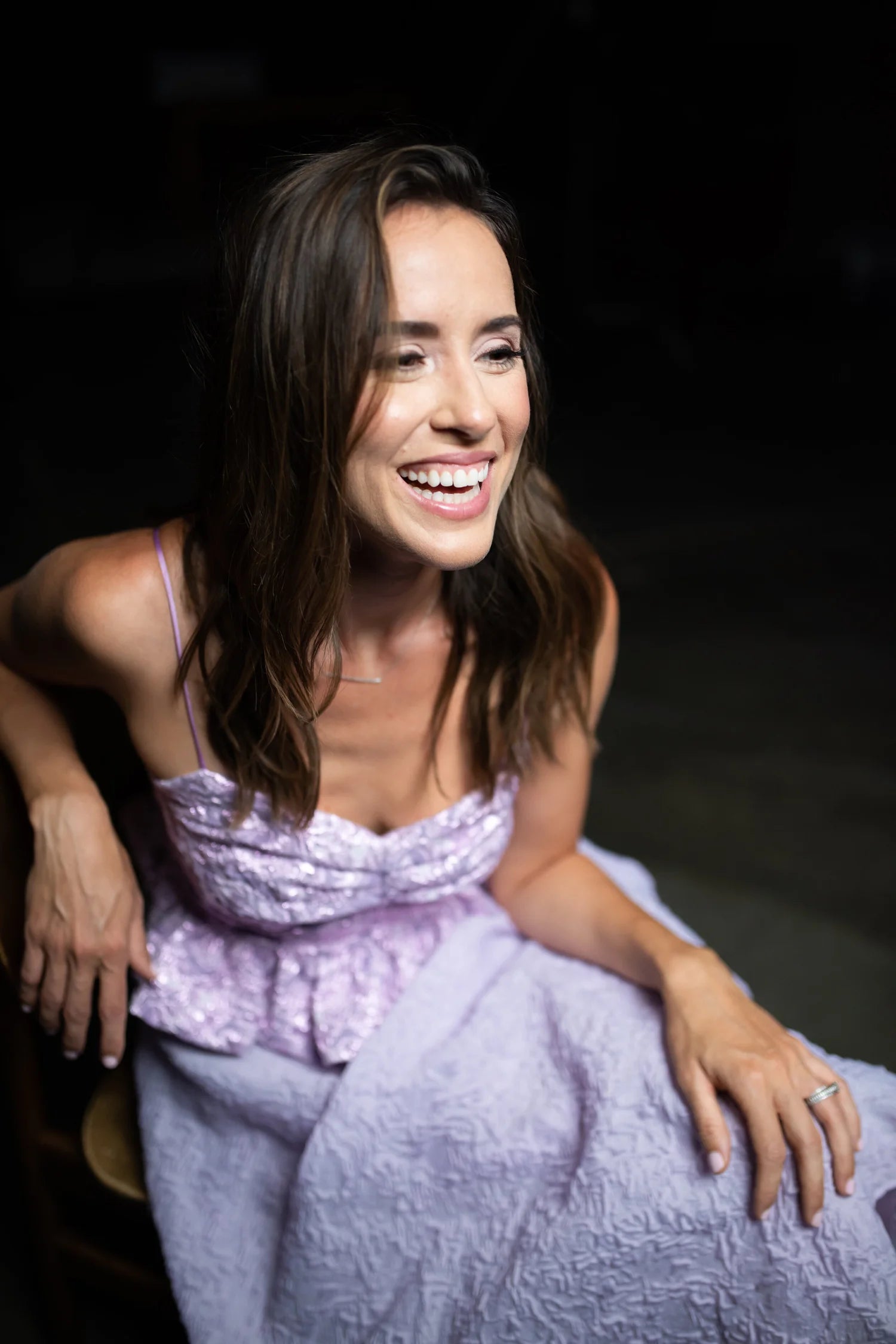 Woman in a light purple dress sitting against a dark background