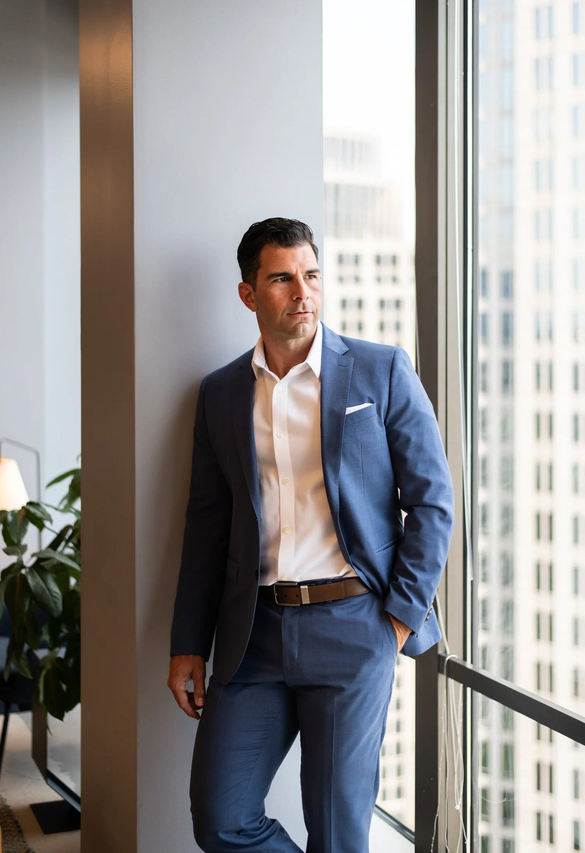 Man in a blue suit standing by a window with cityscape view