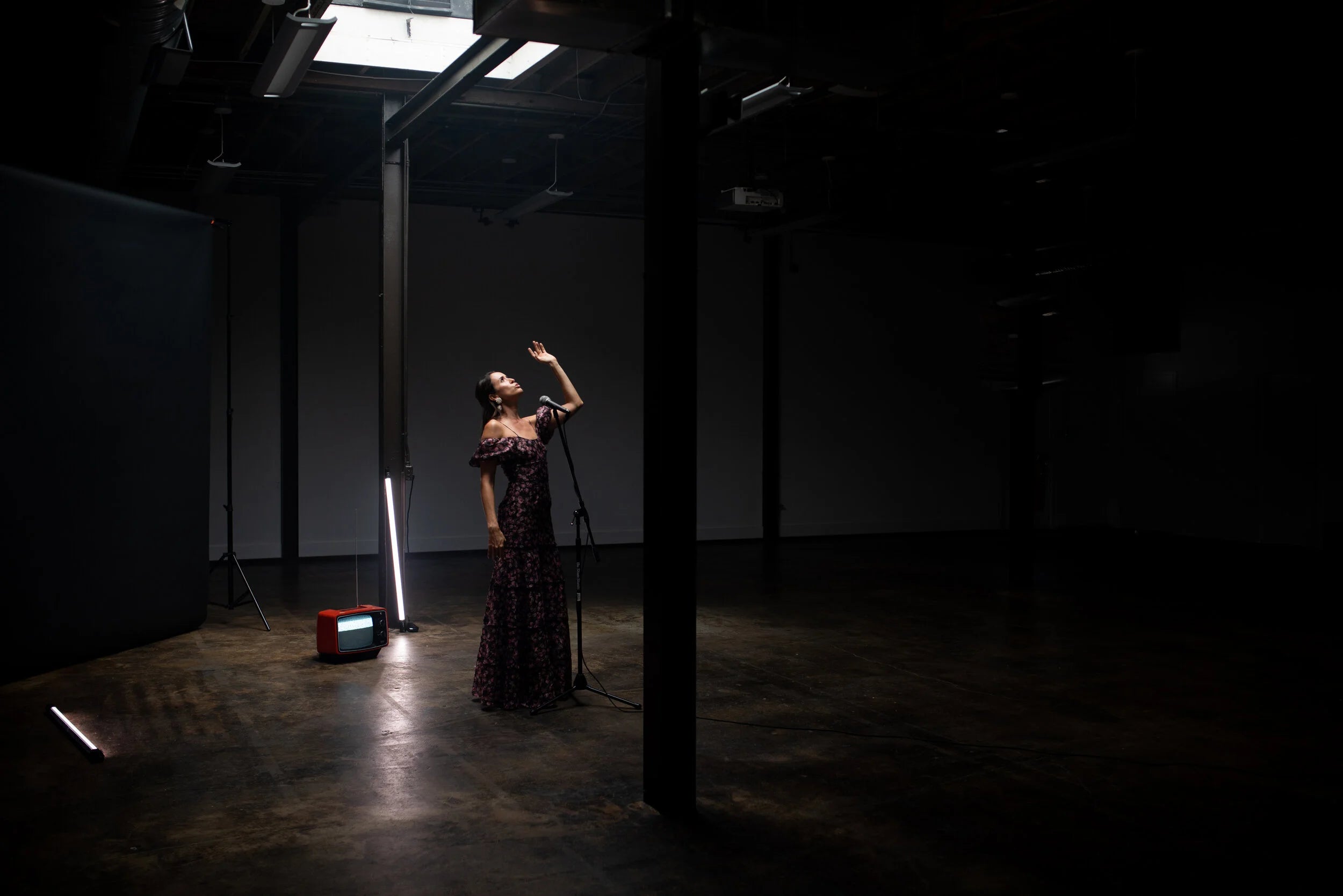 Person in a dark room with minimal lighting, standing near a microphone stand.