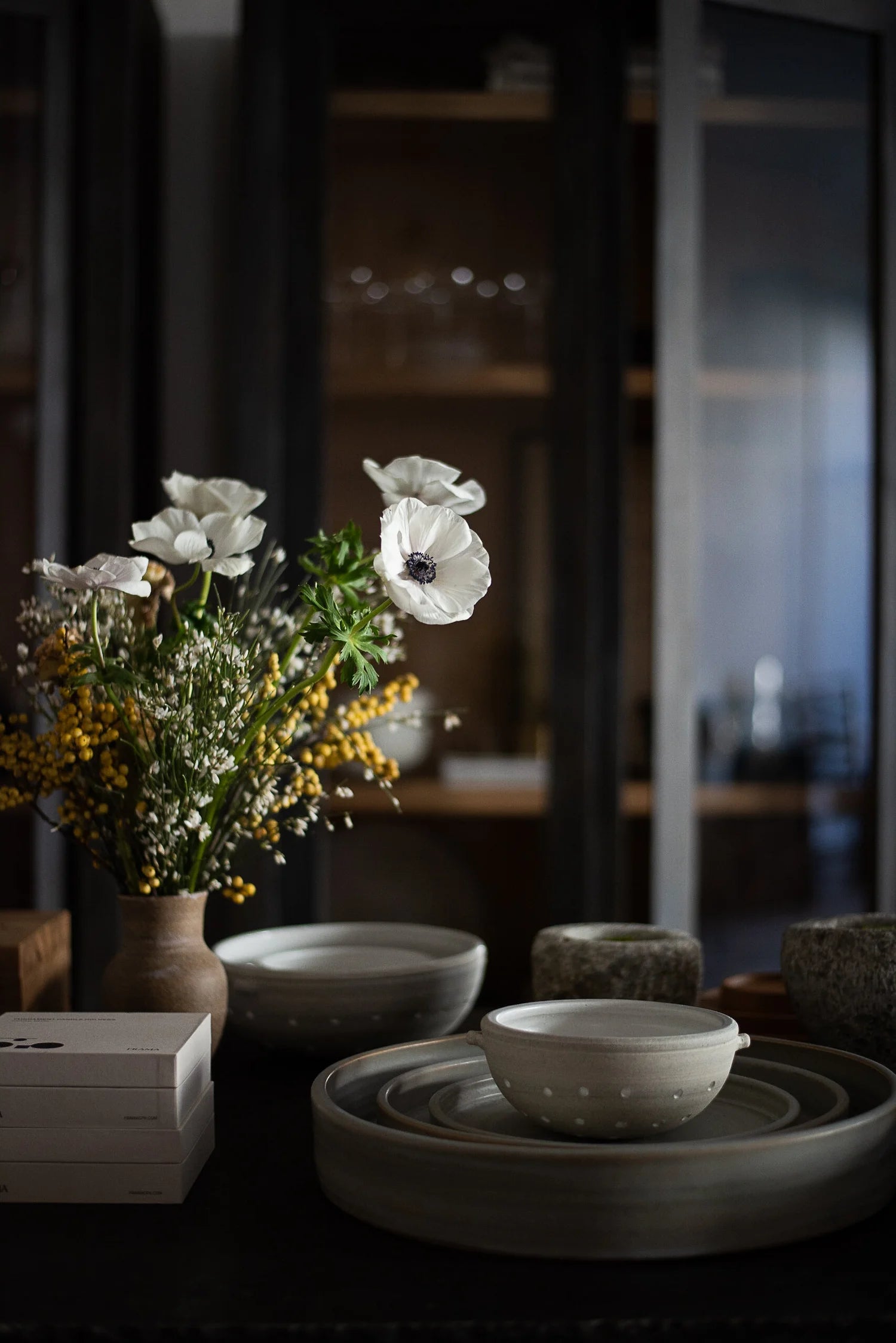 Ceramic bowls and a vase with flowers on a dark surface, blurred background